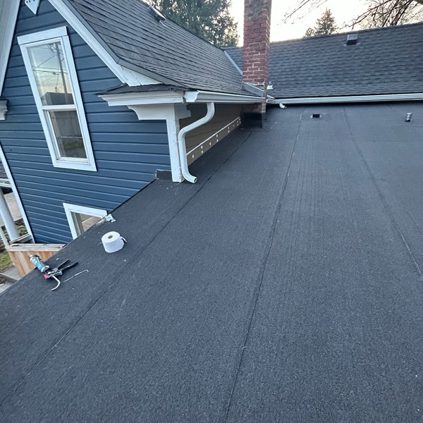 Finished low slope roof section next to a blue sided house